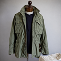 Olive green military field jacket with stand collar, four flap pockets and drawcord waist